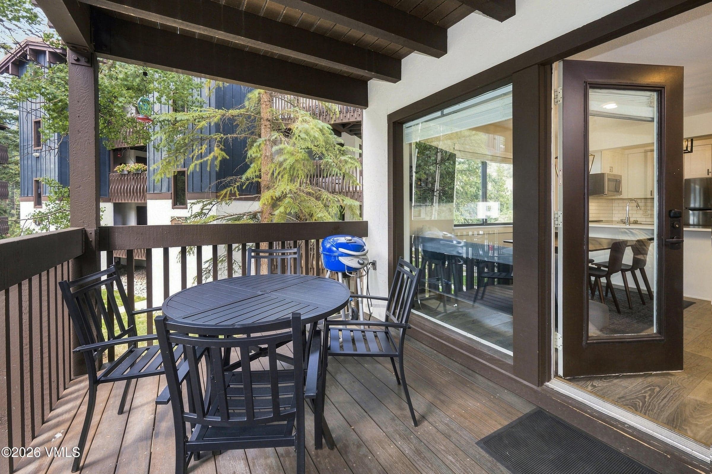 Covered private deck off the living area with dining table and gas grill.