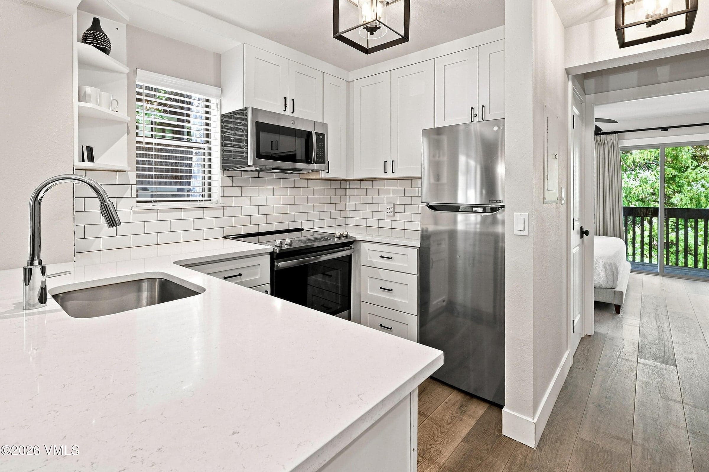 Kitchen with stainless refrigerator, quartz counters, and open sightline to bedroom hallway.
