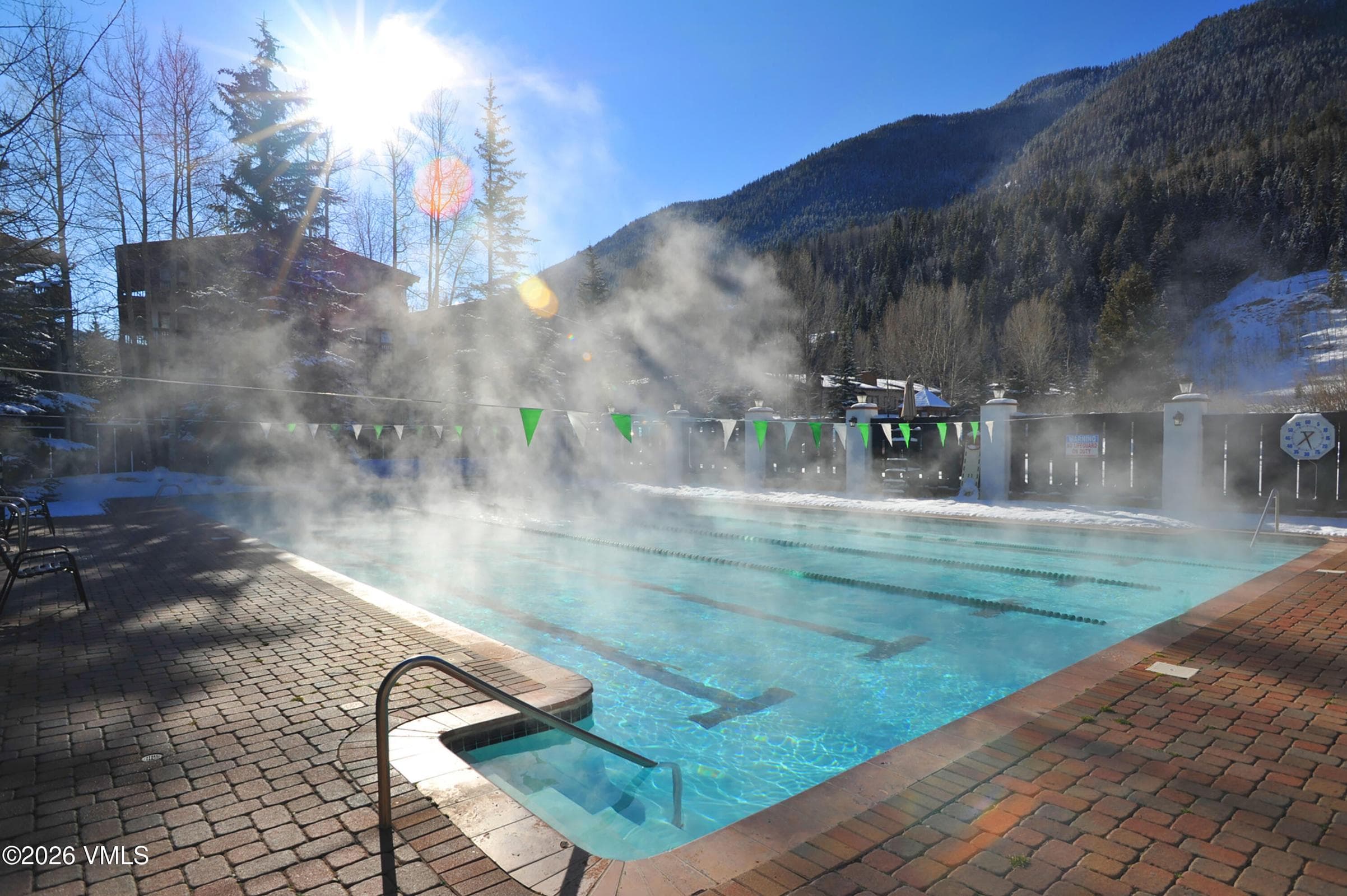 Heated pool and hot tub with steam rising, winter mountain backdrop.